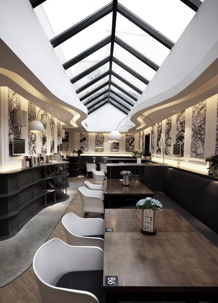 Café-restaurant Liang Dian à Changzhou : salle sous verrière, tables en bois sombre, chaises blanches et murs ornés de tableaux, design d’intérieur par le studio Camille Brunot