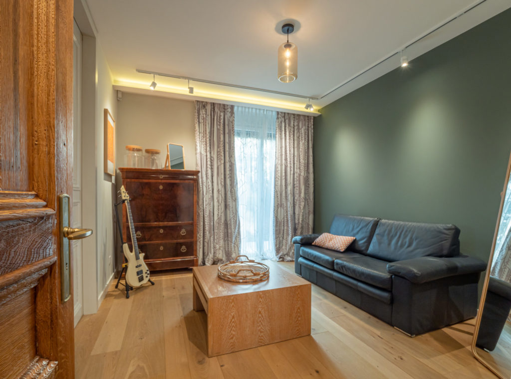 Salon de l’appartement La Gradelle à Genève, mur vert profond, canapé en cuir et table basse en bois, Camille Brunot