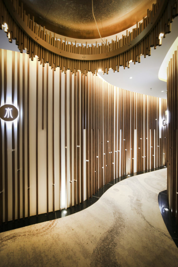 Design d’intérieur sur mesure : couloir courbe habillé de lames verticales en bois rétroéclairées, plafond doré et sol en marbre, par le studio Camille Brunot